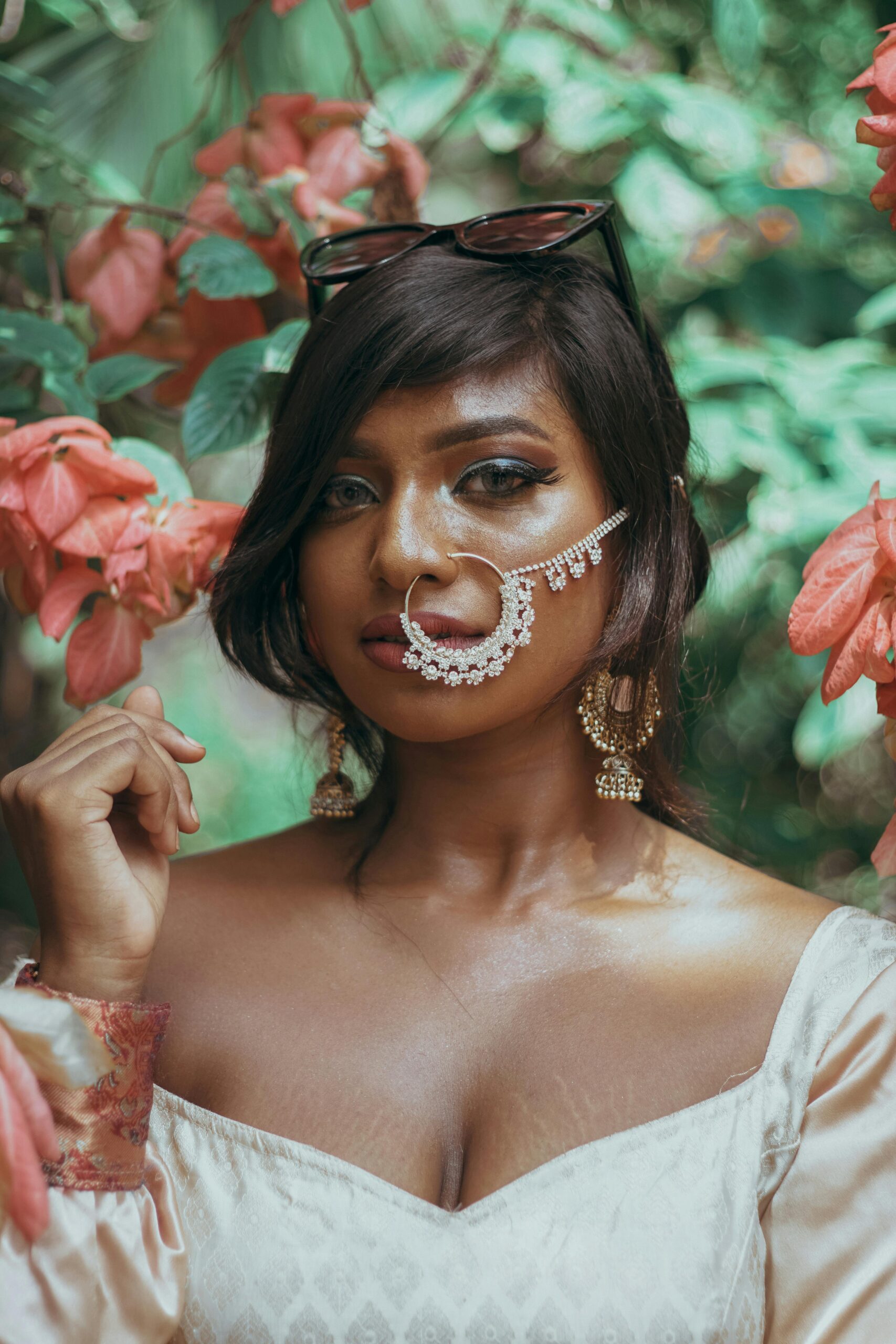 Stunning portrait of a woman with traditional nose jewelry surrounded by lush red and green foliage.